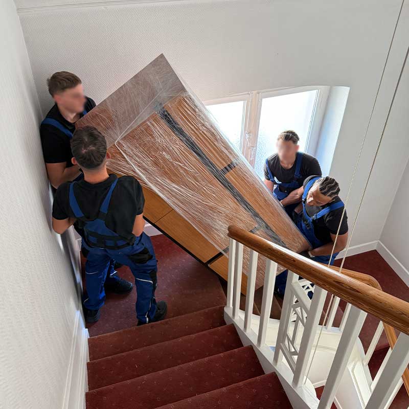Umzugshelfer tragen ein verpacktes Möbelstück durch ein Treppenhaus beim Umzug