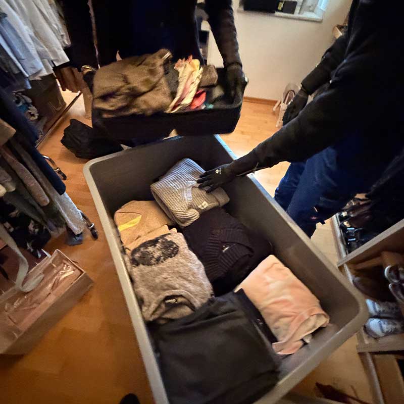 Umzugshelfer verpacken Kleidung und persönliche Gegenstände in Transportboxen für den Umzug.