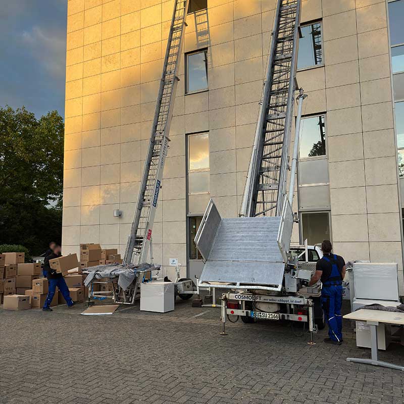 Zwei Möbellifte stehen vor einem mehrstöckigen Gebäude und unterstützen den Transport von Möbeln und Umzugskartons bei einem Umzug.